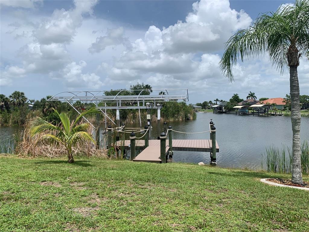 A boat dock with a metal lift structure sits on a canal near a grassy yard — 9500 ATTICA CIRCLE, PORT CHARLOTTE, FL