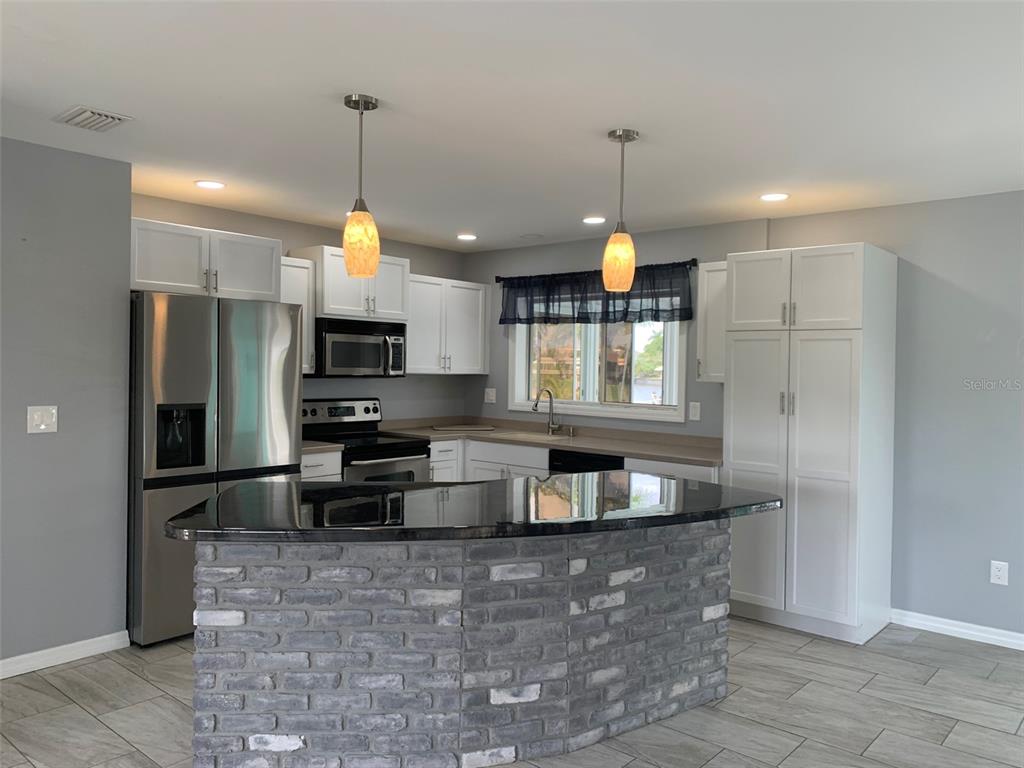 A kitchen features white cabinets, stainless steel appliances, a brick-faced island, and gray tile flooring — 9500 ATTICA CIRCLE, PORT CHARLOTTE, FL