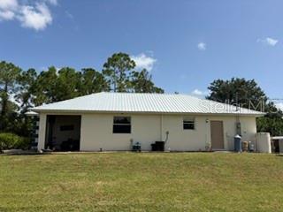 The exterior of a single-story house with a white metal roof and a grassy yard — 12460 HIMALAYA AVENUE, PUNTA GORDA, FL