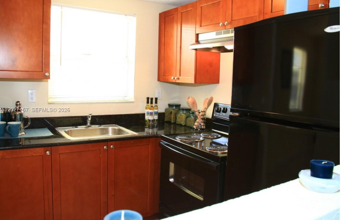 A kitchen features cherry wood cabinets, black countertops, and black appliances — 4271 NW 5th St # 117, Plantation FL 33317, PLANTATION, FL