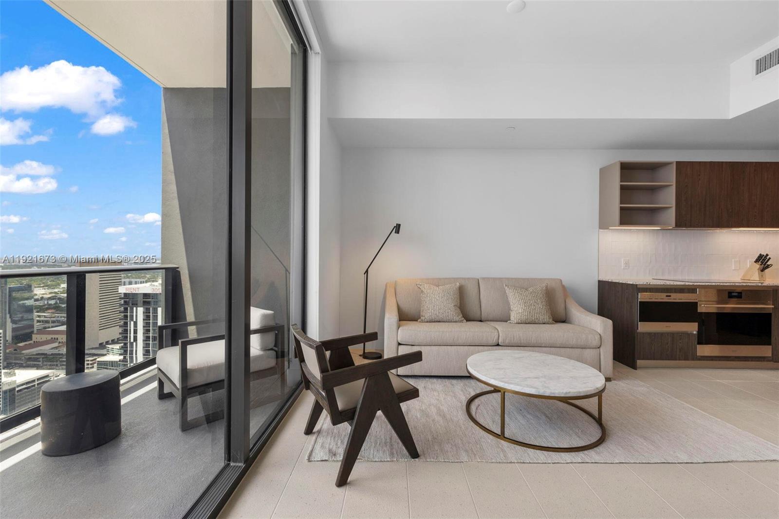 A high-rise balcony features outdoor furniture overlooking a city skyline and a blue bay — 159 NE 6th St # 5008, Miami FL 33132, MIAMI, FL