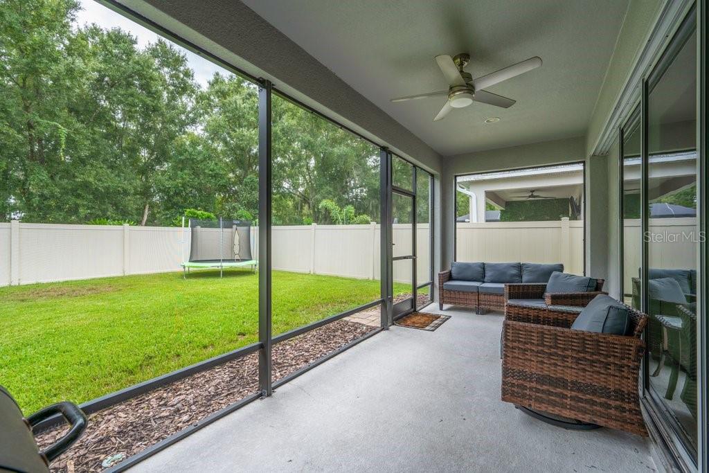A screened-in patio features a concrete floor, wicker furniture, a ceiling fan, and a backyard — 17651 BRIGHT WHEAT DRIVE, LITHIA, FL