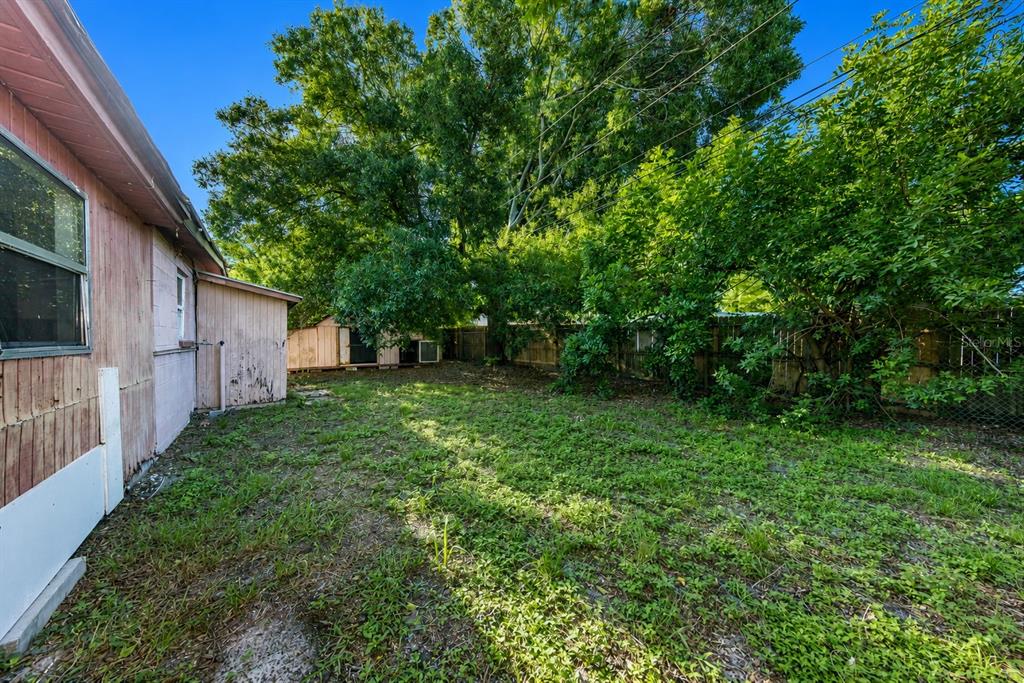 A view of a grassy backyard with a pink house, a shed, and mature trees — 8528 N 92ND TERRACE, SEMINOLE, FL