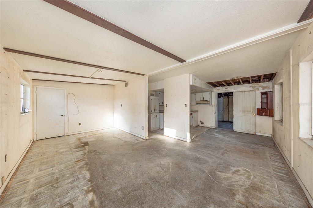 An unfinished room with exposed ceiling beams, concrete flooring, and an adjacent kitchen area — 8528 N 92ND TERRACE, SEMINOLE, FL