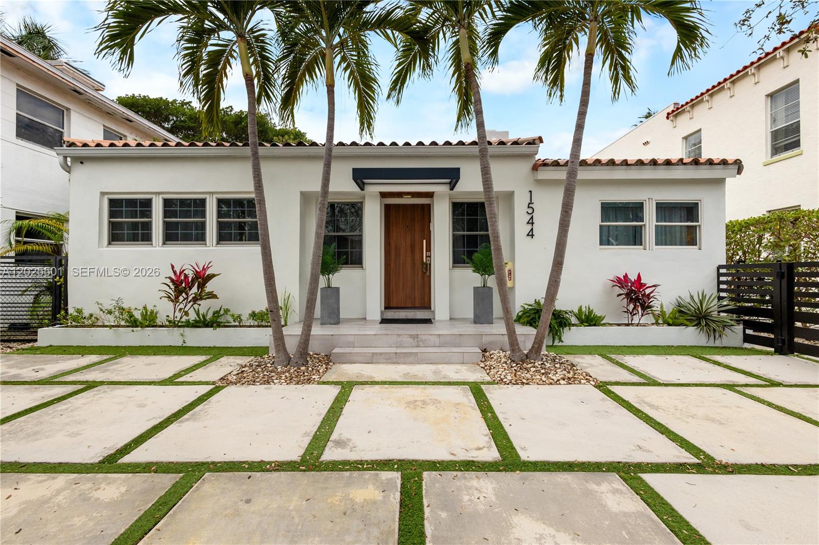 A white single-story house features a wooden front door, palm trees, and concrete pavers — 1544 Michigan Ave, Miami Beach FL 33139, MIAMI BEACH, FL