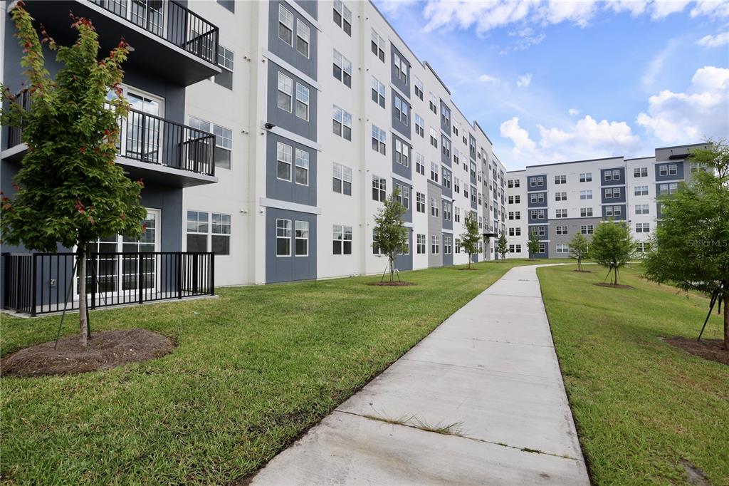 A multi-story apartment building exterior features balconies, a concrete walkway, and landscaped green space — 5579 MILLENIA PARK BOULEVARD UNIT 519, ORLANDO, FL