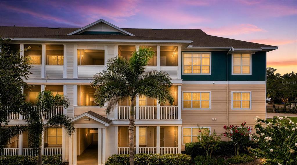 A three-story apartment building exterior features tan siding, white railings, and a palm tree — 4802 51ST STREET W UNIT 1410, BRADENTON, FL