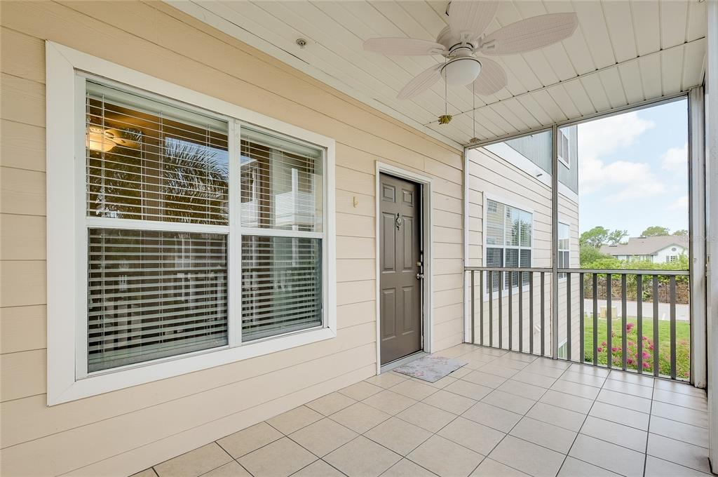 A covered balcony with light-colored tile flooring, a ceiling fan, and a brown entry door — 4802 51ST STREET W UNIT 1410, BRADENTON, FL