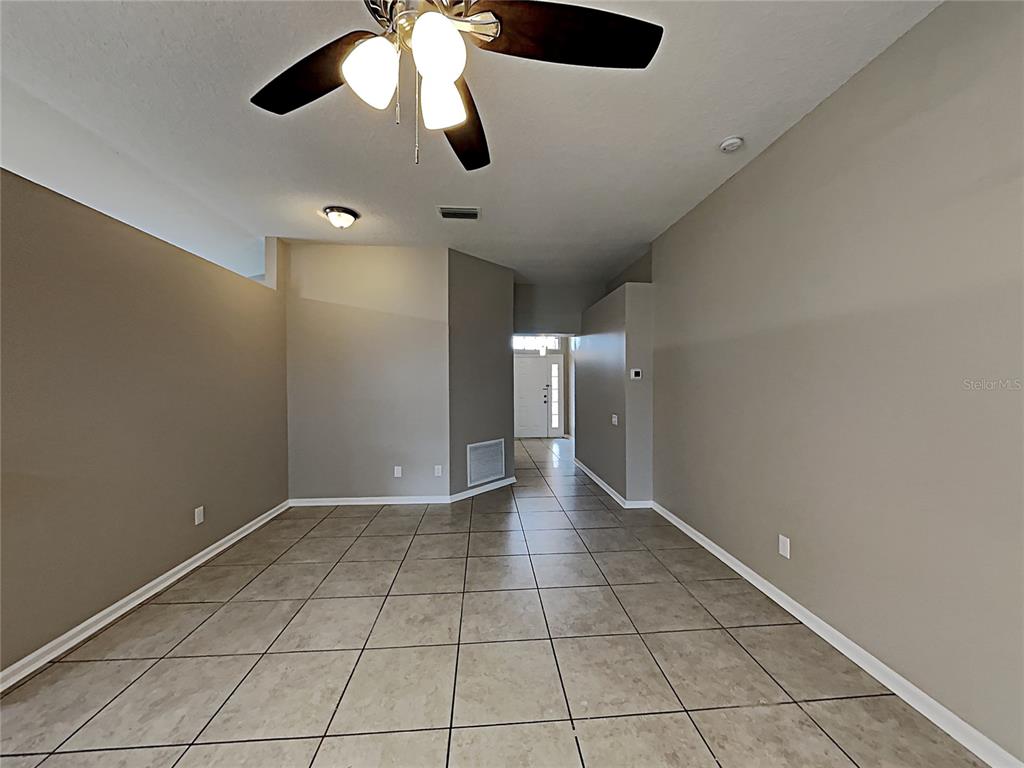 An empty room features beige walls, tiled flooring, a ceiling fan, and a front entryway — 10328 SOARING EAGLE DRIVE, RIVERVIEW, FL