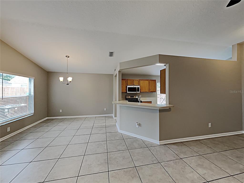 An open-concept dining area with tile flooring connects to a kitchen featuring wood cabinets — 10328 SOARING EAGLE DRIVE, RIVERVIEW, FL