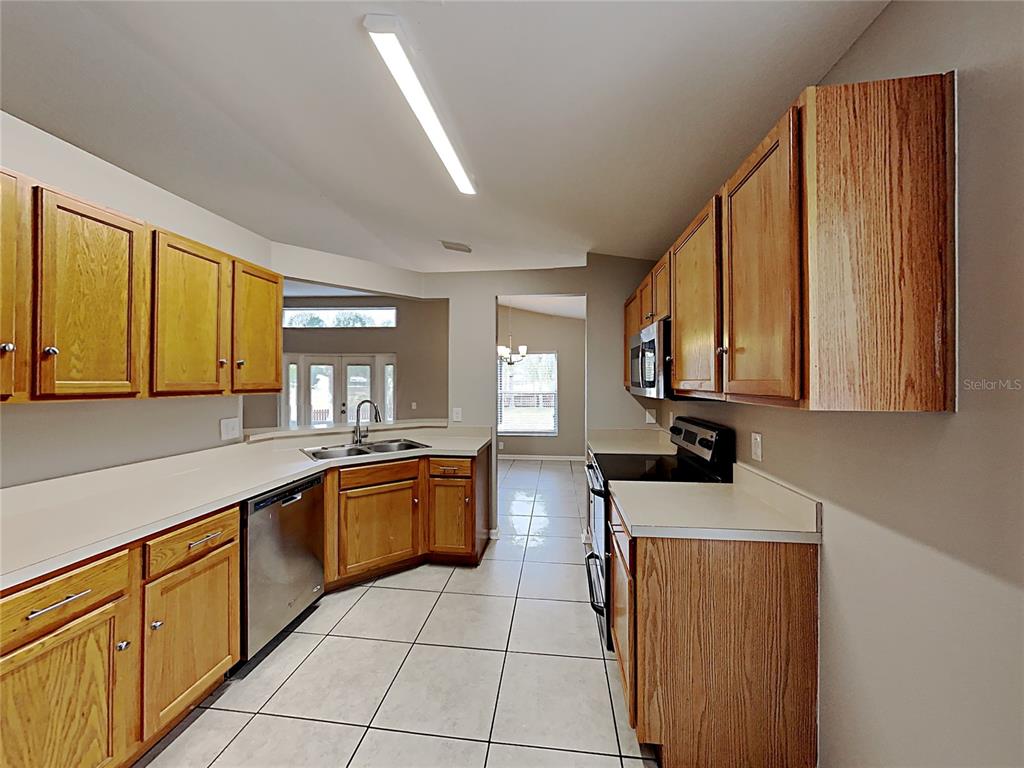 A kitchen features oak cabinets, white countertops, stainless steel appliances, and light-colored tile flooring — 10328 SOARING EAGLE DRIVE, RIVERVIEW, FL