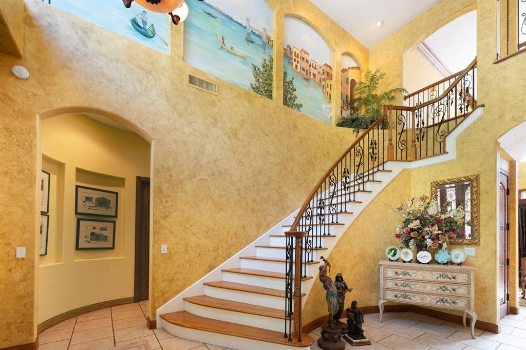 A grand foyer features a curved staircase, textured yellow walls, and a large wall mural — 543 ISLEWORTH CLOSE, TARPON SPRINGS, FL