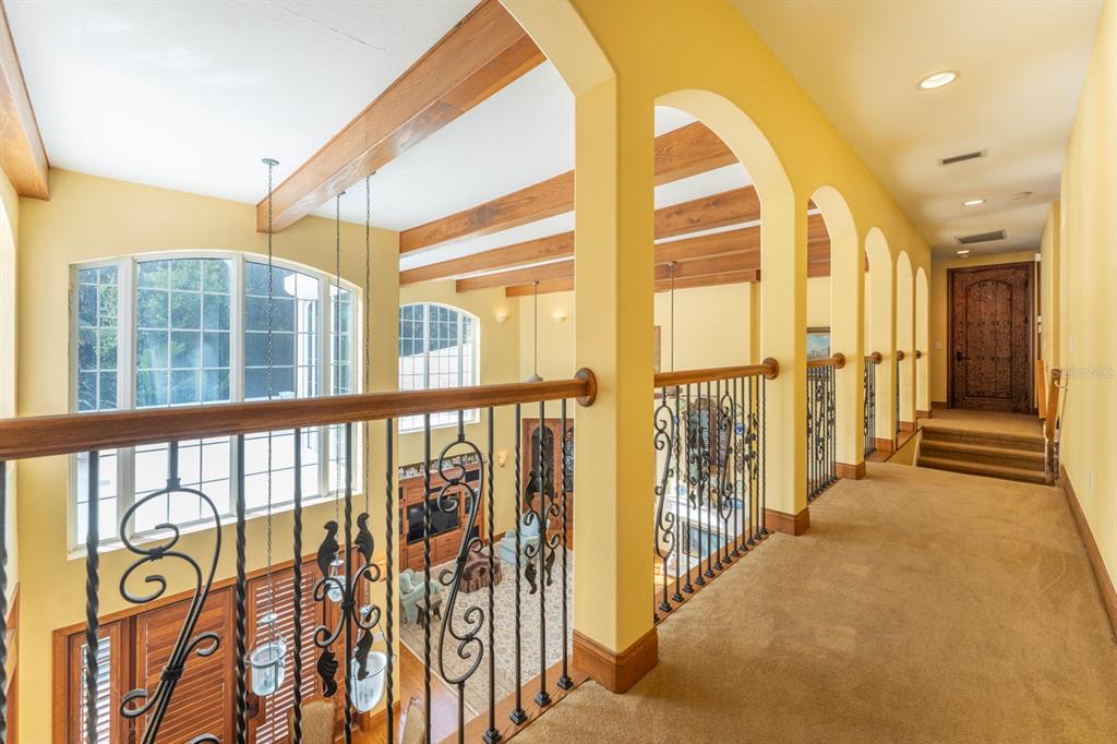 A carpeted hallway with arched openings overlooks a living area with wood ceiling beams — 543 ISLEWORTH CLOSE, TARPON SPRINGS, FL