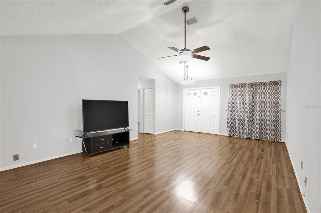A living room with vaulted ceilings, wood-look flooring, a ceiling fan, and a television console — 9 BLACKBERRY PLACE, PALM COAST, FL