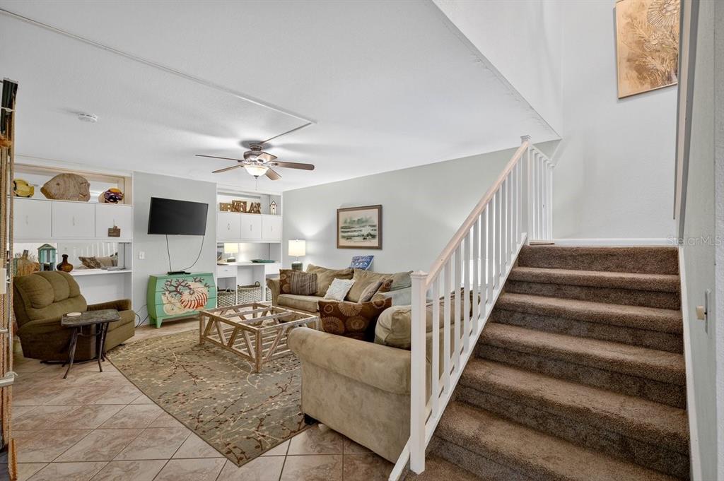 A living room features a staircase, a ceiling fan, a sofa, and a patterned rug — 4150 S ATLANTIC AVENUE UNIT 114B, NEW SMYRNA BEACH, FL