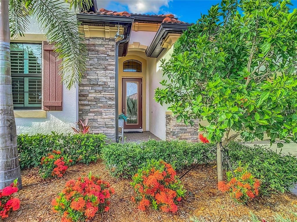 The front entrance of a house features a stone facade, a glass-paneled door, and landscaping — 25025 SPARTINA DRIVE, VENICE, FL
