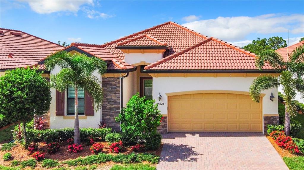 A single-story house with a tiled roof, stone accents, and a two-car garage — 25025 SPARTINA DRIVE, VENICE, FL