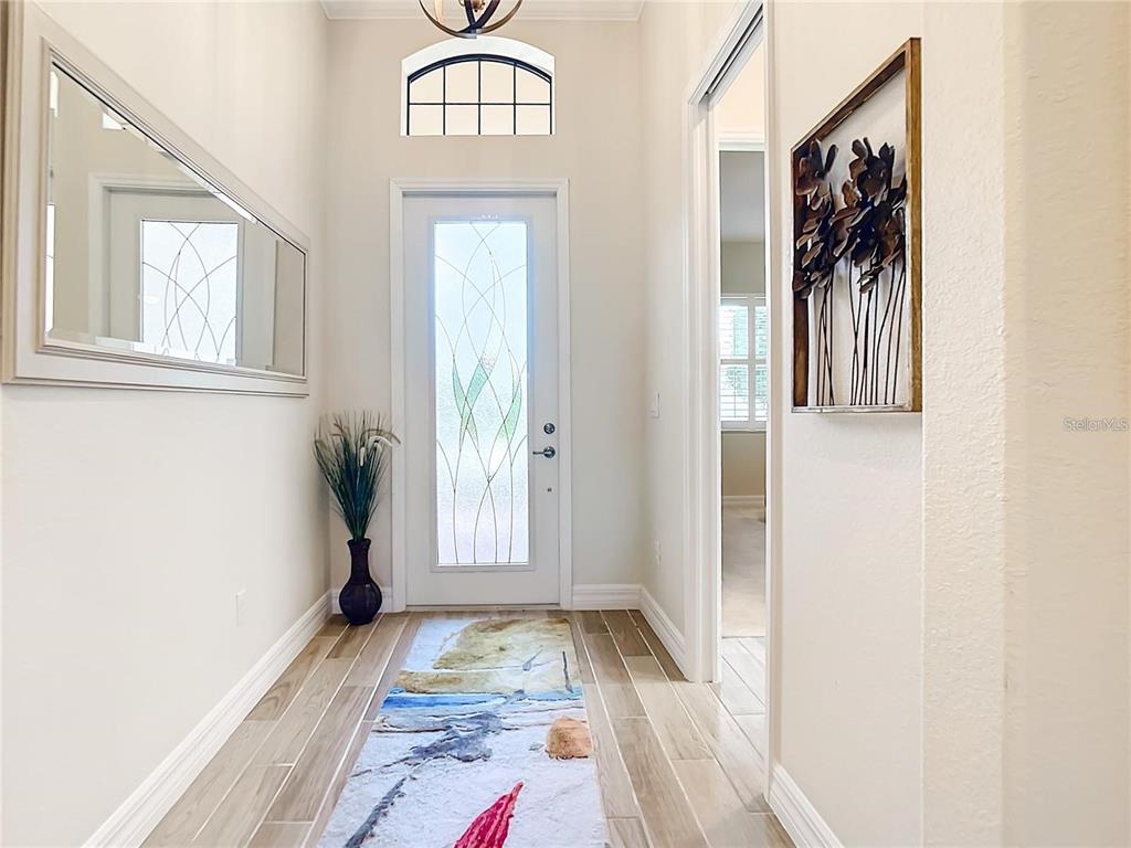 A bright entryway features a glass-paneled front door, wood-look tile flooring, and a large mirror — 25025 SPARTINA DRIVE, VENICE, FL