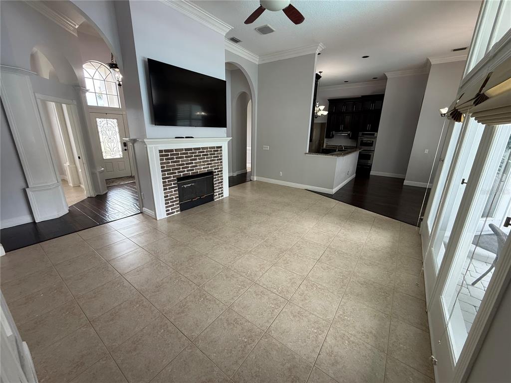 A living room features a brick fireplace, a wall-mounted television, tile flooring, and an adjacent kitchen — 325 LESLIE LANE, LAKE MARY, FL