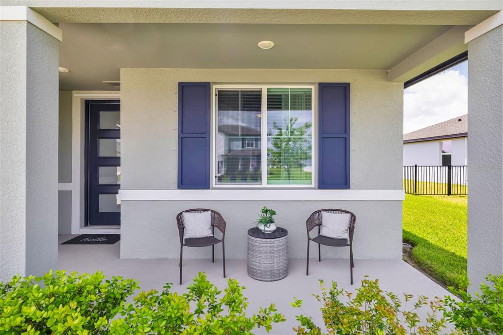 A covered front porch features two chairs, a small table, and blue window shutters — 14086 GINNIE SPRINGS WAY, PARRISH, FL
