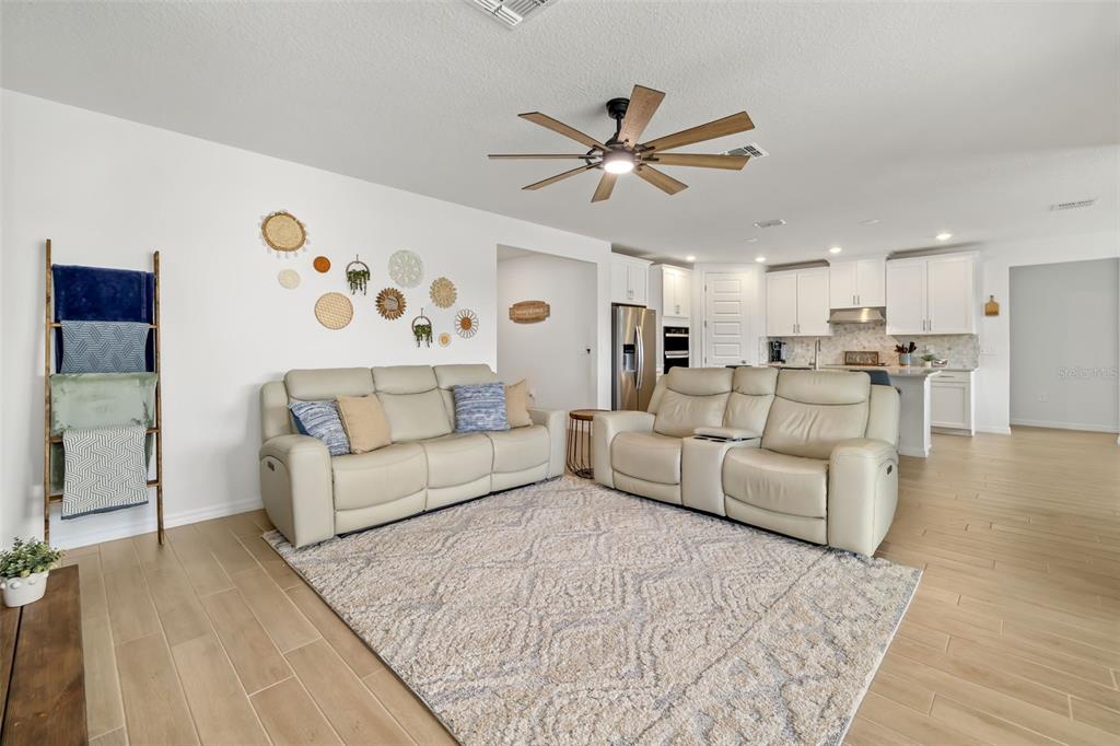 A living room with light-colored sofas, a patterned area rug, and an open-concept kitchen — 14086 GINNIE SPRINGS WAY, PARRISH, FL
