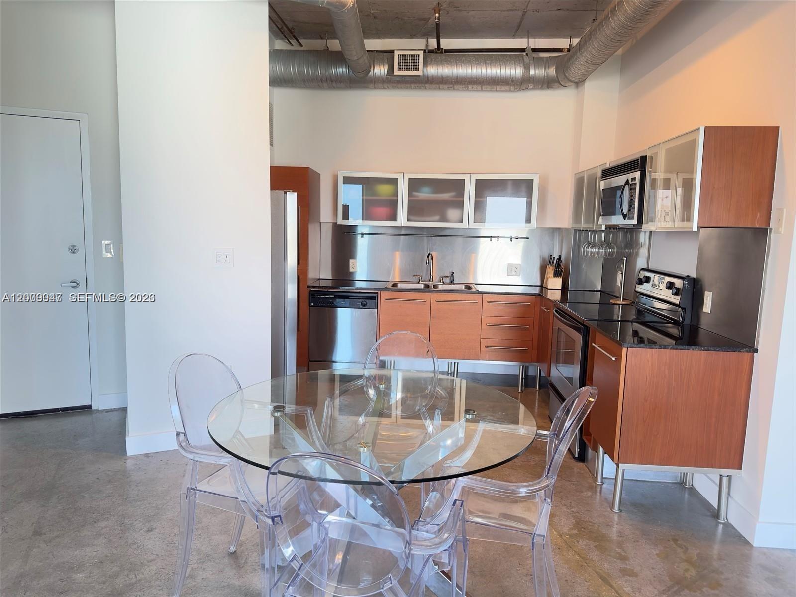 A kitchen features wood cabinets, stainless steel appliances, and a glass dining table with chairs — 10 SW South River Dr # 1607, Miami FL 33130, MIAMI, FL