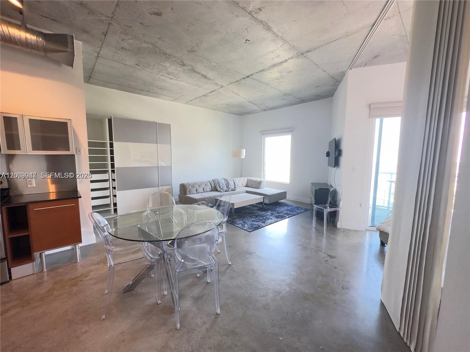 An open-concept living and dining area features concrete ceilings, polished floors, and modern furniture — 10 SW South River Dr # 1607, Miami FL 33130, MIAMI, FL