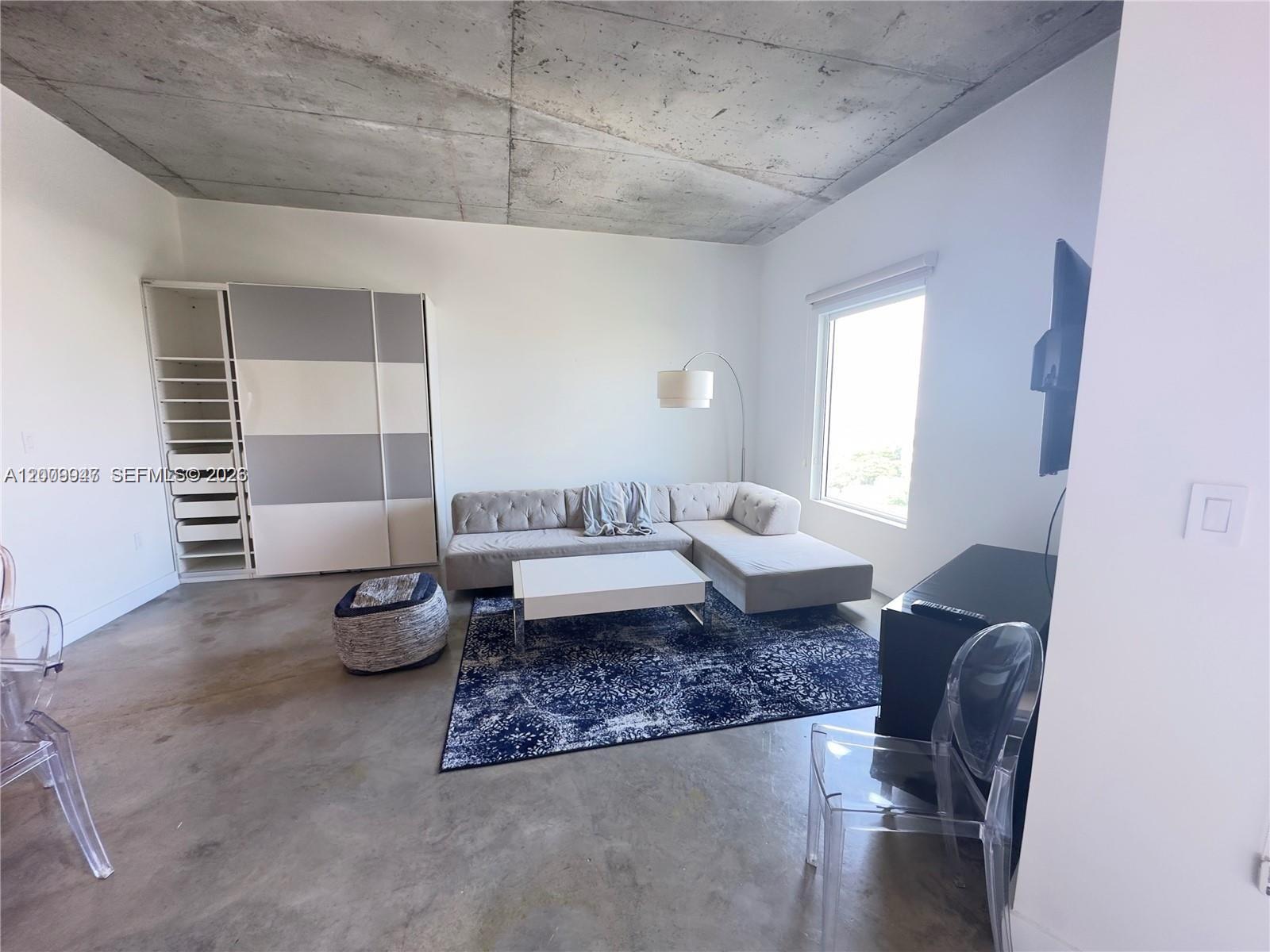 A modern living room features a concrete ceiling, gray sectional sofa, and a patterned rug — 10 SW South River Dr # 1607, Miami FL 33130, MIAMI, FL