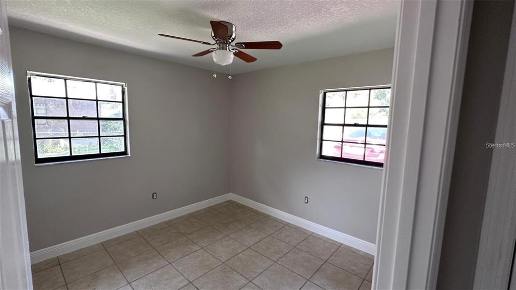 An empty bedroom features light gray walls, tile flooring, and a ceiling fan — 210 N LONE OAK DRIVE UNIT 1, LEESBURG, FL