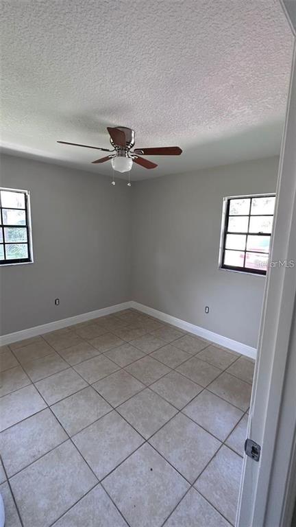 An empty room features light gray walls, a ceiling fan, and beige tile flooring — 210 N LONE OAK DRIVE UNIT 1, LEESBURG, FL