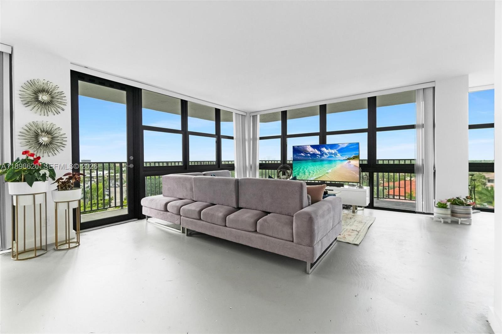 A living room features a grey sectional sofa, a television, and floor-to-ceiling windows — 1000 Parkview Dr # 809, Hallandale Beach FL 33009, HALLANDALE BEACH, FL