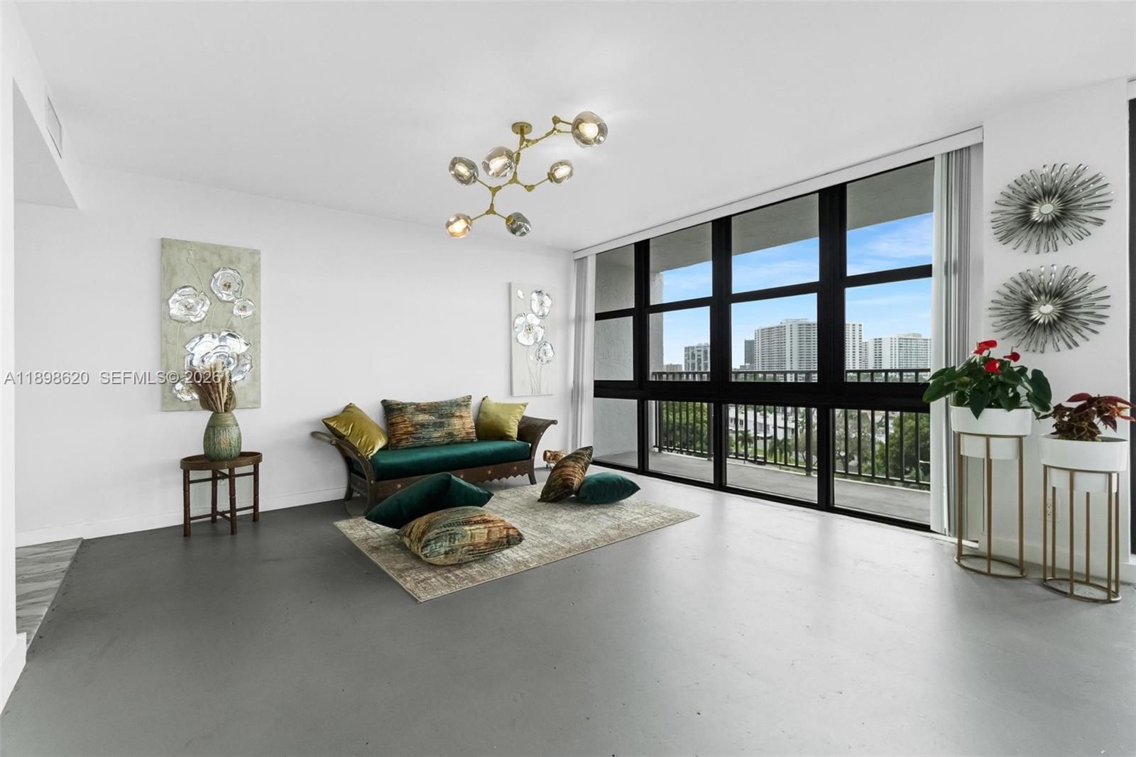 A living room features a green sofa, a modern chandelier, and floor-to-ceiling windows — 1000 Parkview Dr # 809, Hallandale Beach FL 33009, HALLANDALE BEACH, FL
