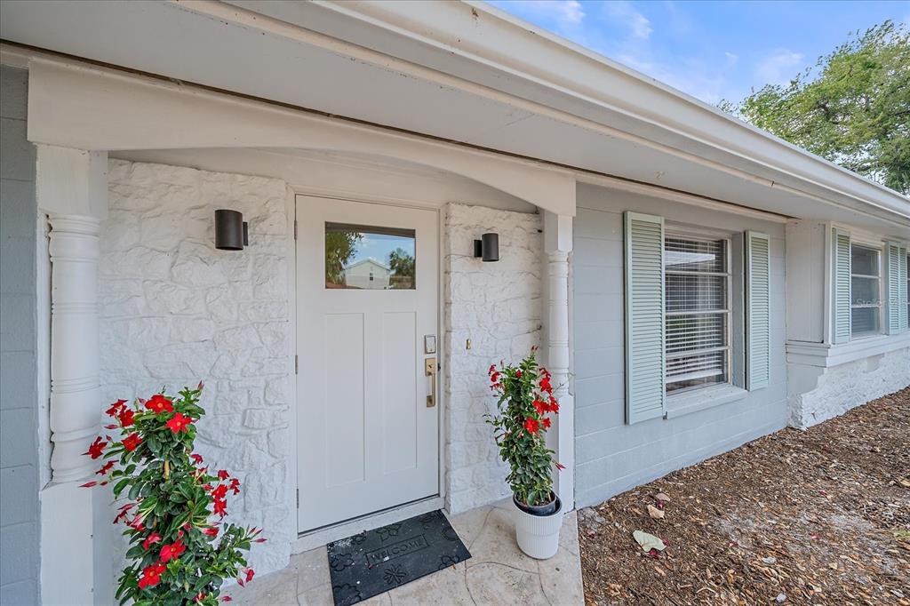 A white front door is centered between two potted red flowers on a stone porch — 611 VENICE LANE, SARASOTA, FL