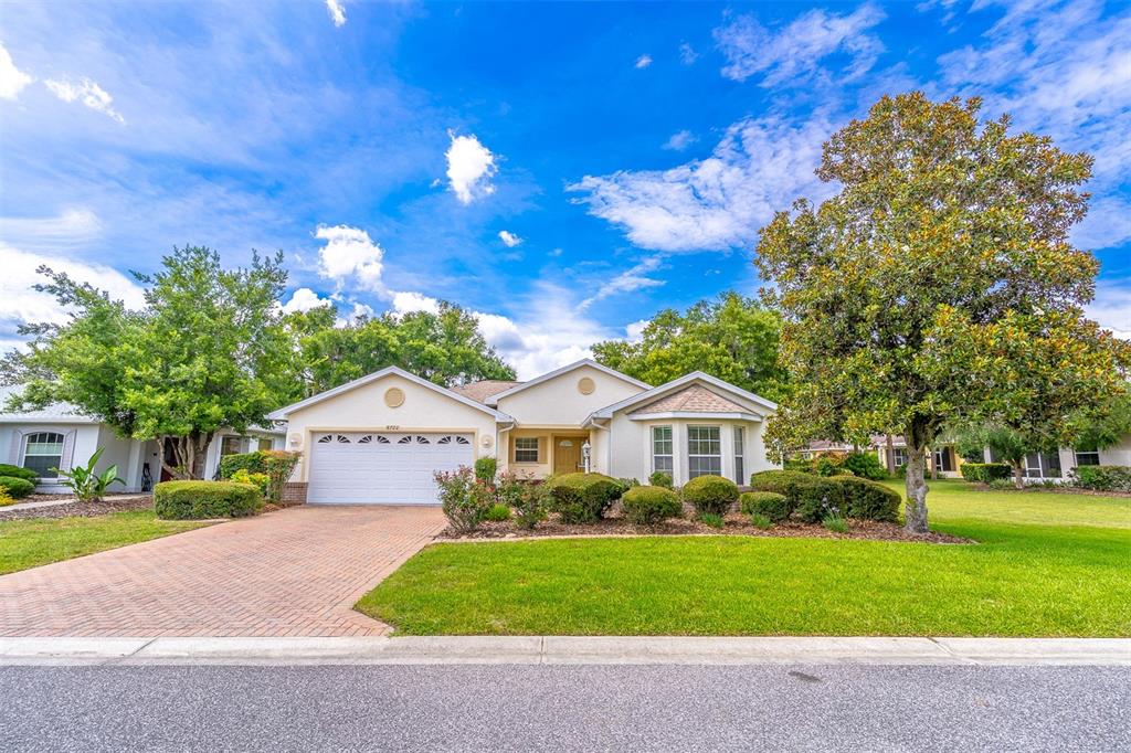 A single-story house with a brick driveway, white garage door, and a large front tree — 8722 SW 83RD LOOP, OCALA, FL