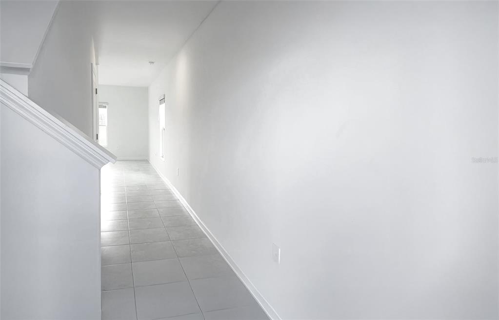 A long, narrow hallway features white walls, light-colored tile flooring, and a staircase railing — 1658 TEAGAN LANE, WINTER HAVEN, FL