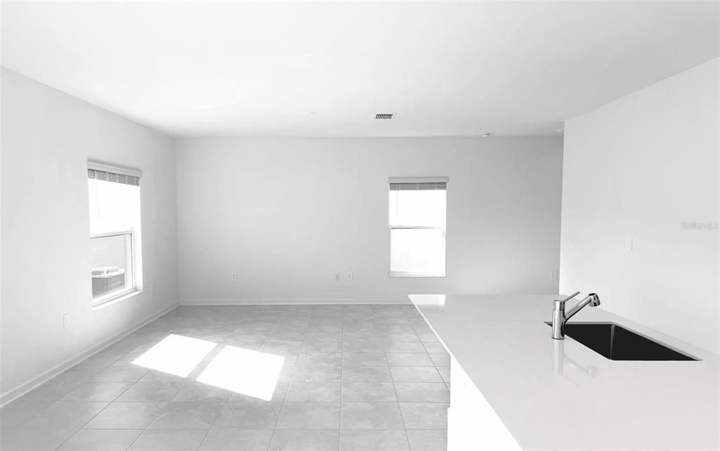 A bright, empty room with light tile flooring, white walls, and a kitchen island sink — 1658 TEAGAN LANE, WINTER HAVEN, FL
