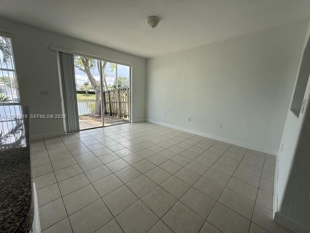 An empty room with light-colored tile flooring and a sliding glass door leading outside — 11419 NW 76th Ter, Doral FL 33178, DORAL, FL