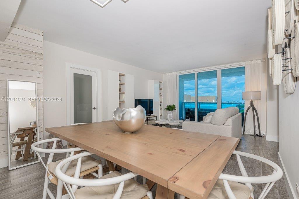 A dining area with a wooden table and white chairs opens into a living room — 2301 Collins Ave # 926, Miami Beach FL 33139, MIAMI BEACH, FL
