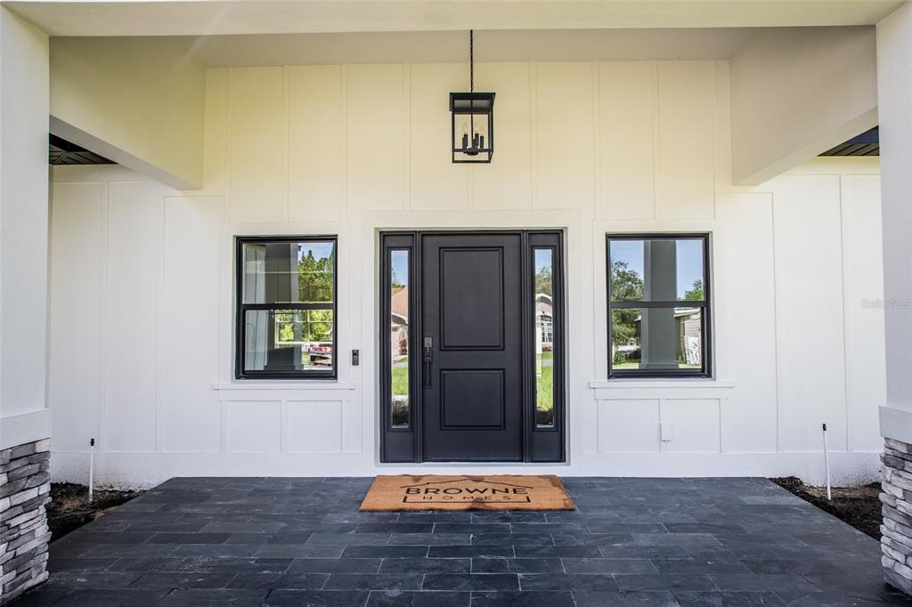 The exterior front entrance features a dark door, black-framed windows, and a stone-tiled porch — 18080 MABERLY ROAD, WEEKI WACHEE, FL