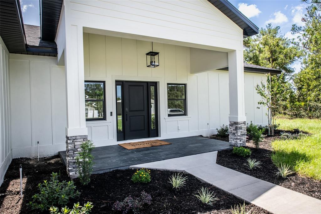 A modern white home exterior features a covered porch, stone-based columns, and a black door — 18080 MABERLY ROAD, WEEKI WACHEE, FL