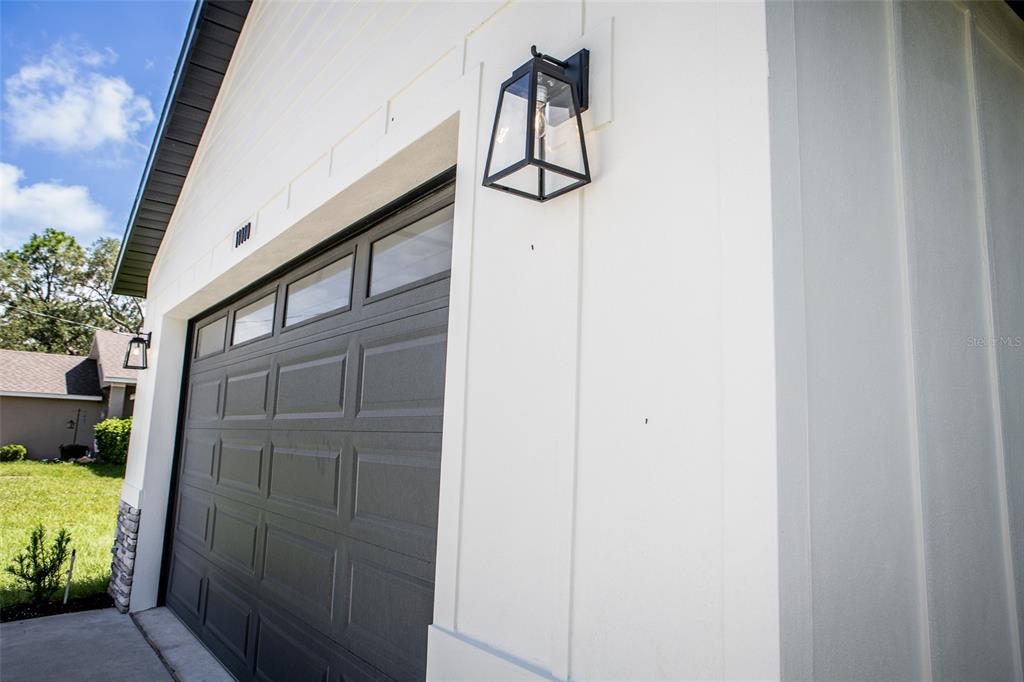A close-up view of a white exterior wall with a black garage door and lantern — 18080 MABERLY ROAD, WEEKI WACHEE, FL