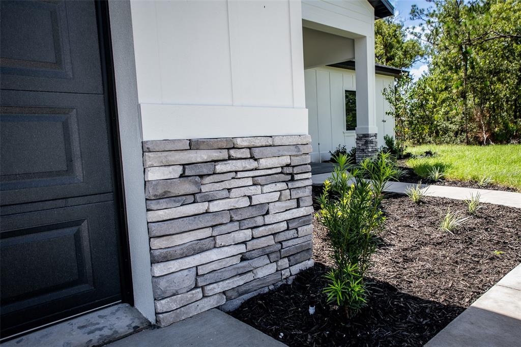 A stone-veneer base accents the white exterior wall next to a dark garage door — 18080 MABERLY ROAD, WEEKI WACHEE, FL