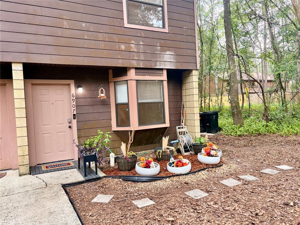 The exterior of a two-story brown house features a front door, bay window, and planters — 6907 SW 44TH AVENUE, GAINESVILLE, FL