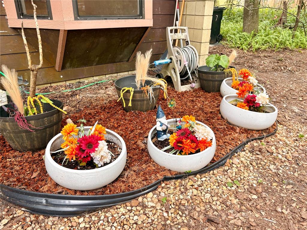 A collection of potted plants and flowers sits on mulch in front of a house — 6907 SW 44TH AVENUE, GAINESVILLE, FL