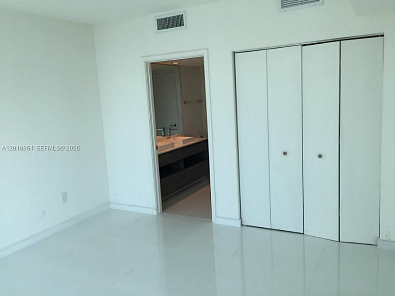 A bedroom with white walls, glossy tile flooring, a closet, and an attached bathroom — 1100 S MIAMI AV # 3302, Miami FL 33130, MIAMI, FL