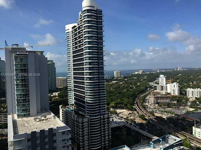 An aerial view shows a tall, modern residential skyscraper surrounded by other buildings and greenery — 1100 S MIAMI AV # 3302, Miami FL 33130, MIAMI, FL