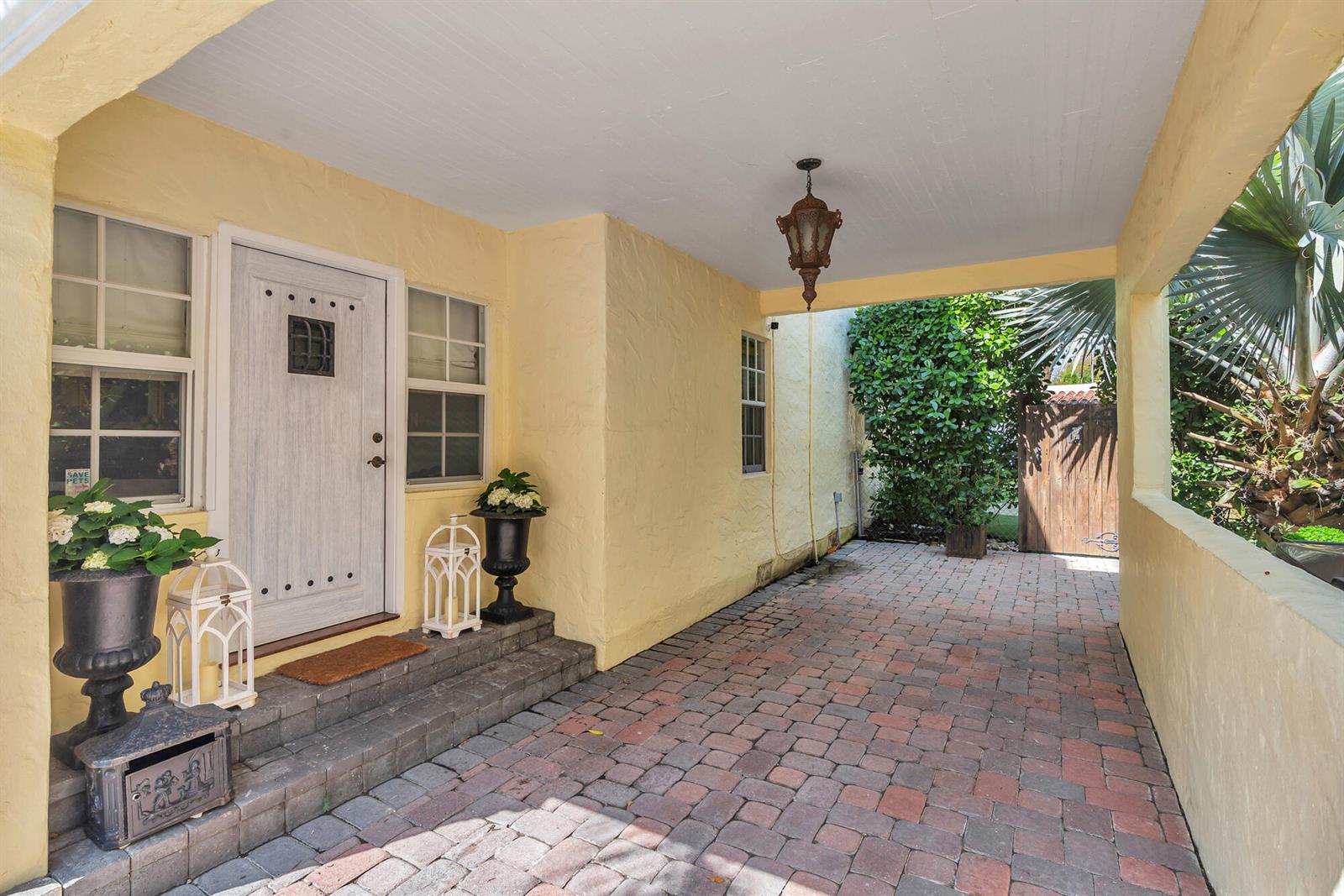A covered brick patio leads to a yellow stucco house with a white front door — 3213 Vincent Road, West Palm Beach FL 33405, WEST PALM BEACH, FL