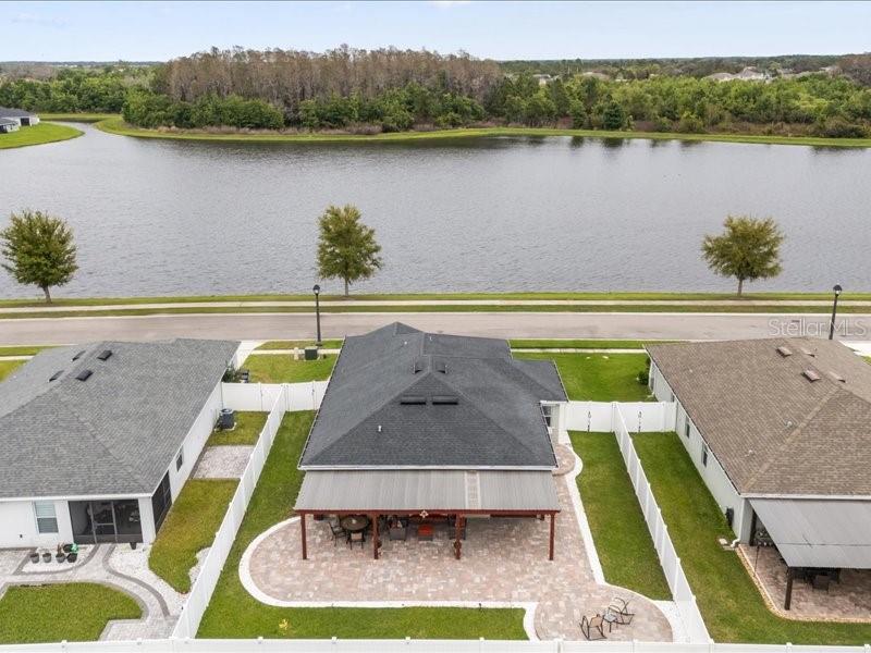 An aerial view shows three houses with back patios and white fences facing a lake — 2962 HARLOW AVENUE, ST CLOUD, FL