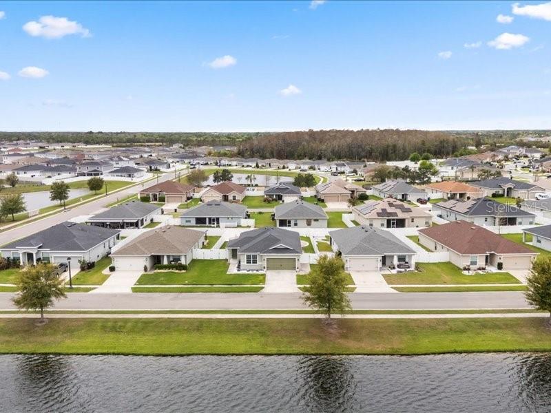 An aerial view shows a suburban neighborhood with single-family homes bordering a large pond — 2962 HARLOW AVENUE, ST CLOUD, FL