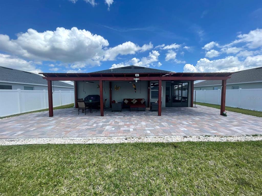 A covered patio with a paver floor sits behind a house with a white fence — 2962 HARLOW AVENUE, ST CLOUD, FL